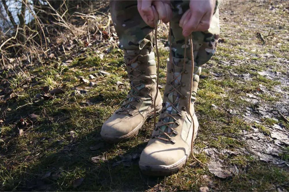 A soldier in camouflage pants lace up army boots