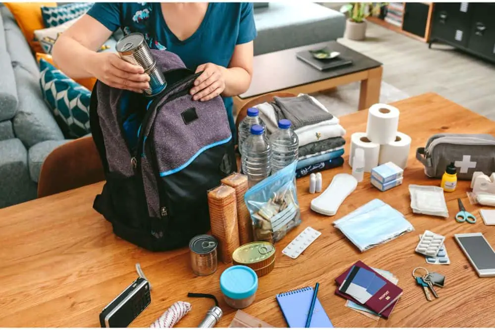 woman putting cans of food to prepare emergency backpack in living room